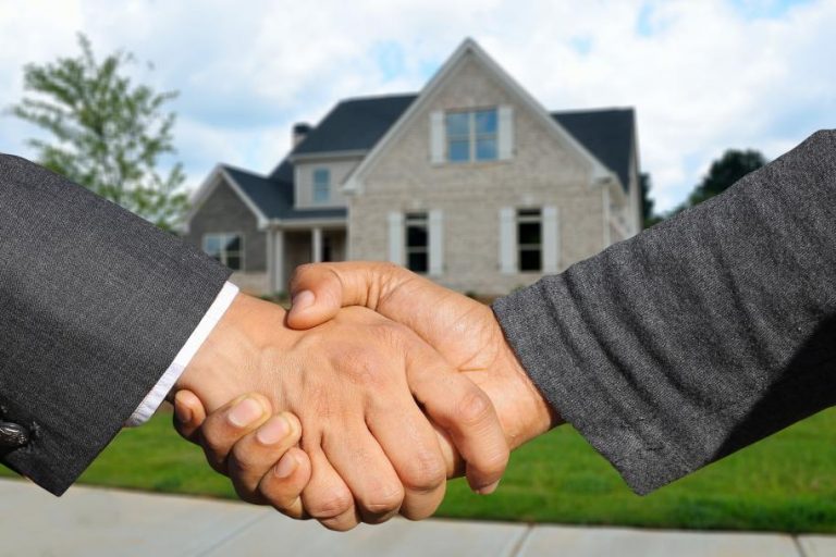 Two people handshaking in front of a house
