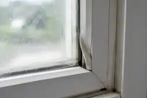 Cloudy window glass sits beside a warped white vinyl frame and darkened seals.